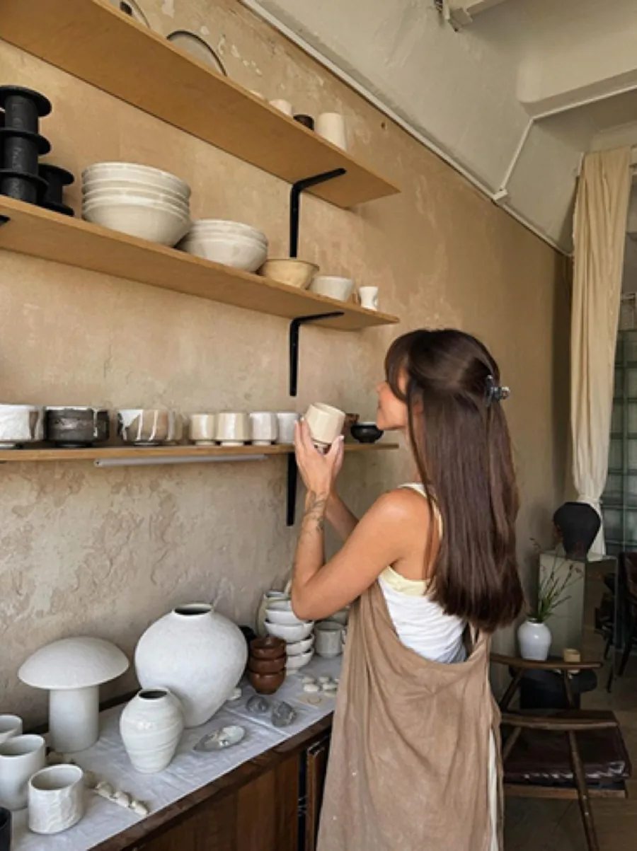 Ceramicist reaching for handmade tableware on studio shelving